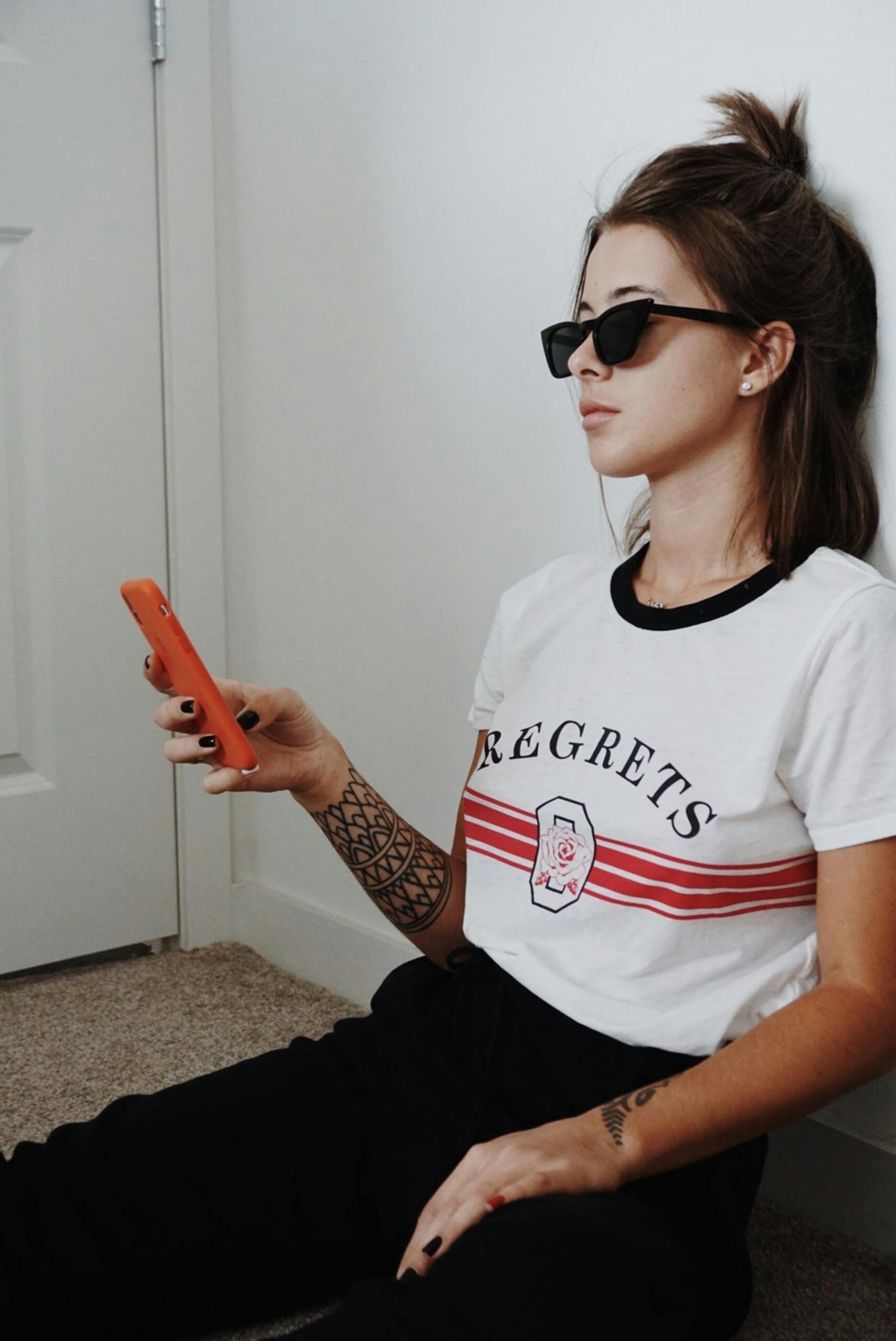 A fashionable young woman with sunglasses and tattoo, using a smartphone indoors.